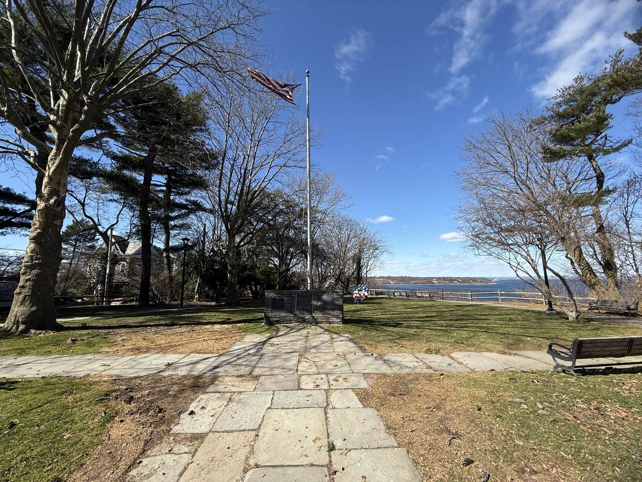 Veterans Memorial Park in Sea Cliff, with trees, a flagpole, and Hempstead Harbor beyond